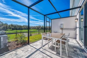 Outdoor screened-in patio with dining table at an Eagle Trace resort residence overlooking a vast golf course.
